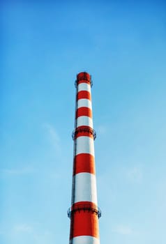 Factory chimney against blue sky background. Vertical shot.