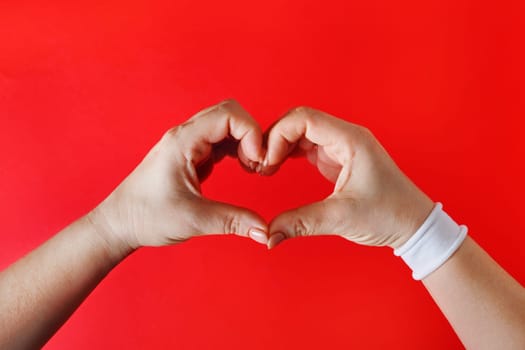 Female hands with white bracelet in the form of heart on red backgroung. Woman hands making heart sign.