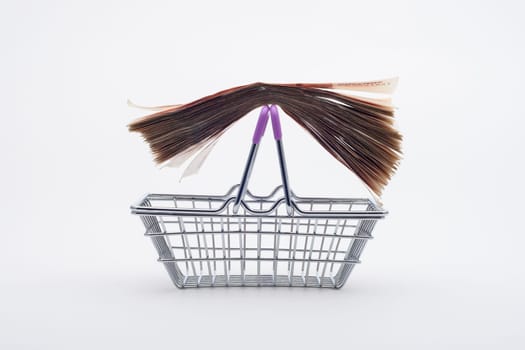 A large stack of paper bills is on the handles of a grocery basket, front view