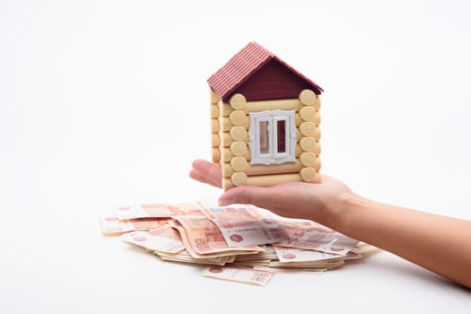 A hand holds a house over a bundle of Russian five-thousandth bills