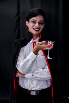 Portrait of asian young adult teenage man wear Halloween costume cloth hold glass of cocktail for Halloween party background. Halloween celebrate and international holiday concept.