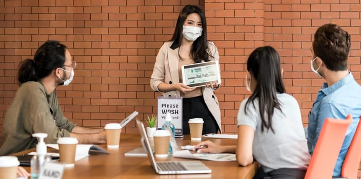 Panoramic shot of Asian business woman present her work in meeting for brainstorm. They wear protective face mask in new normal office preventing coronavirus COVID-19 spreading. Web banner suitable.