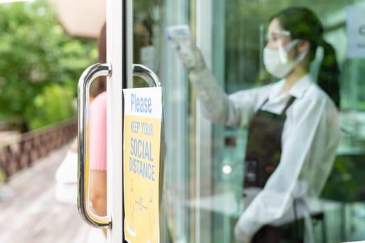Social distance signage for new normal restaurant with asian waitress taking temperature to customer in background. New normal restaurant lifestyle concept.