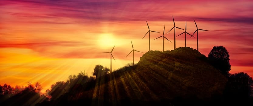 Horizontal composition of seven modern wind farms in the distance on a hill against the backdrop of a beautiful sunset in the evening as a background