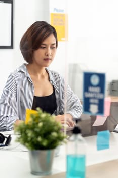 Businesswoman working in home office with social distance using screen partition to prevent from coronavirus COVID-19 spreading. New normal concept after pandemic.