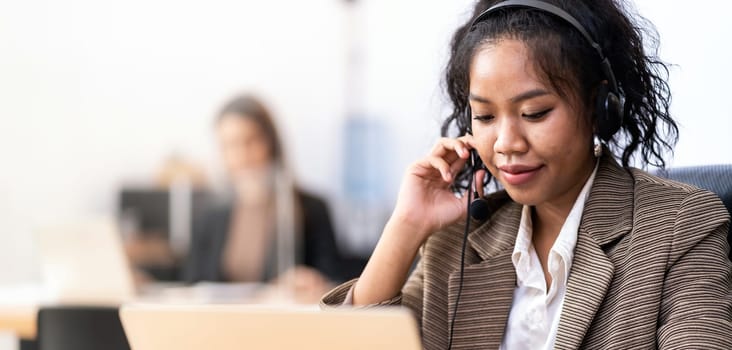 Panorama Young adult friendly confidence operator Mixed race of African asian woman with headsets working in a call center with her colleague in background. Call center and telemarketing sale concept.