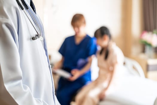 Close up doctor with stethoscope visiting patient in ward with blurred background of nurse taking care of little girl in bed of patient room. Medical health care concept.
