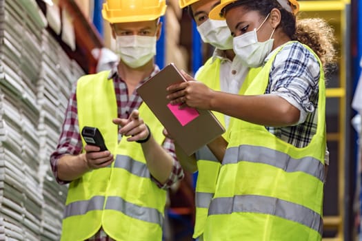 Interracial team Asian African Caucasian working on inventory use barcode scanner and digital tablet in distribution center. They wear face mask prevent from COVID-19. Warehouse and hygiene concept.