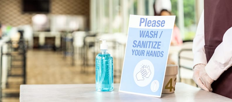 Panorama close up of asian waitress stand with Alcohol gel or hand sanitizer with its signage in new normal restaurant. New normal and hygiene for restaurant lifestyle concept.