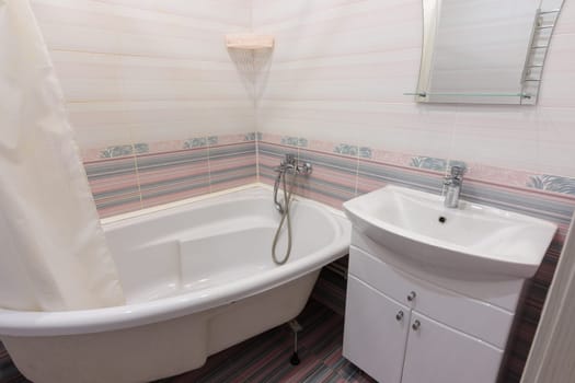 Interior of a cozy ordinary bathroom with a washbasin, a bathtub and a mirror