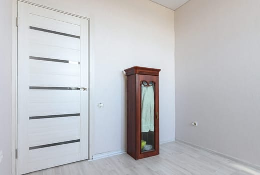 A fragment of a small bedroom in an apartment with poor furniture, a view of the front door and a locker