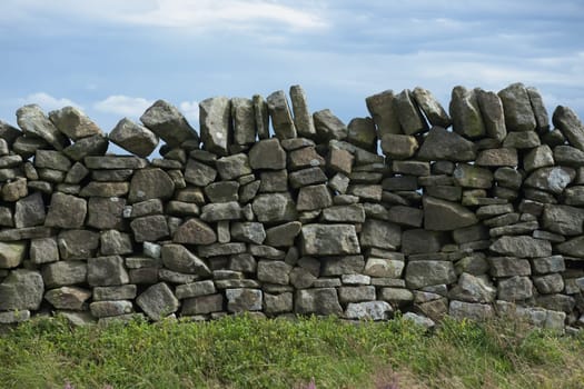 3 - Plain abstract background texture of dry stone wall. Close up of random mix of stone brickwork. Cloudy background and plants in foreground.