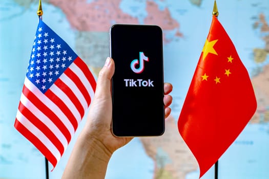 Calgary, Alberta, Canada. Sep 8, 2020. A person holding an iPhone with the TikTok app screen next to a USA and China flags on a world map.
