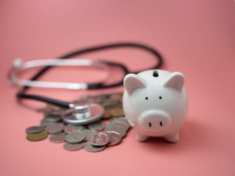 Stethoscope on the pile of money and piggy bank on pink background..Financial health check concept, debt and finance crisis.