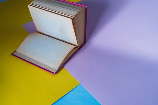 Open book with blank pages placed on a vibrant geometric background of yellow, purple, and blue paper. Creative and artistic concept for literature, writing, or education themes