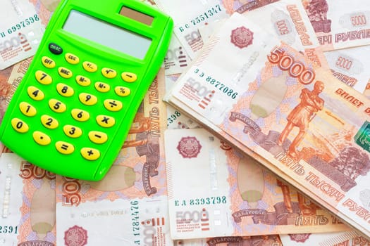 Against the background of money is a calculator and a pack of five thousandth Russian rubles
