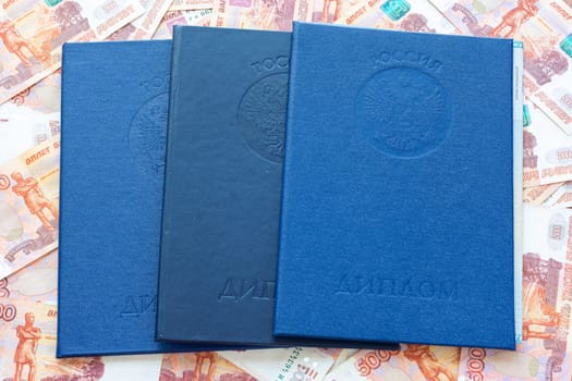 Three higher education diplomas lie against the background of five thousandth bills