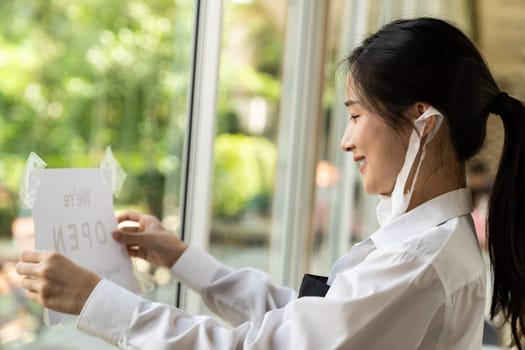 Asian female waitress putting on open signage with social distance for new normal restaurant. New normal restaurant lifestyle concept.