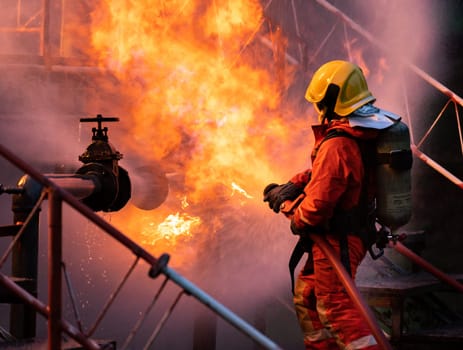 Firefighter using water fog type fire extinguisher to fighting with the fire flame from oil pipeline leak and explosion on oil rig and natural gas station. Firefighter and industrial safety concept.