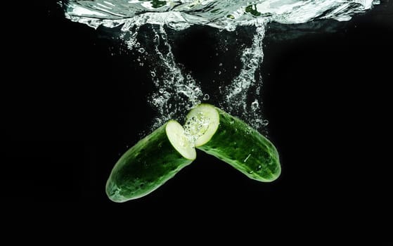 Cucumber cut in half splashing water isolated onblack background. Healthy food concept
