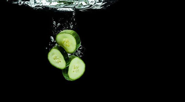 Sliced bio cucumber splashing water isolated on black background. Skin moisturizing cosmetics concept