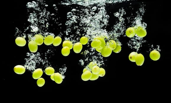 White grape berries splashing into water against black backdrop. Splash photography.