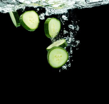 Sliced bio cucumber splashing water isolated on black background. Skin moisturizing cosmetics concept