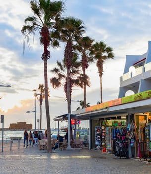 PAPHOS, CYPRUS - FEBRUARY 15, 2019: Touristic downtown embankment with souvenir shops and cafes, car, palm trees and sunset over the sea