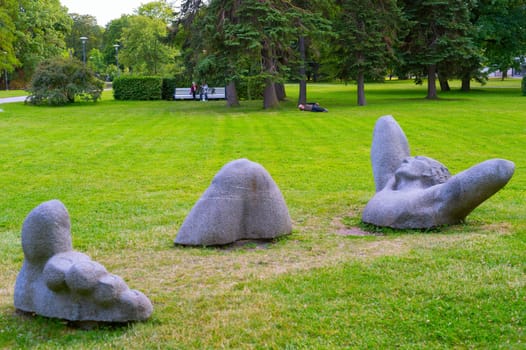 TALLIN, ESTONIA - JULY 15, 2019: People rest in a city park with modern sculpture in the foreground