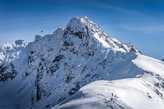 View from Kasprowy Wierch on adventurers climbing on Swinica mountain peak at winter. Tatra Mountains range with snow capped mountain peaks, Poland