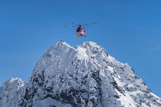 Rescue helicopter saved mountain climbers. People on the top of Swinica steep and rocky mountain peak at winter, Tatra Mountains, Poland