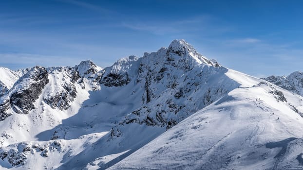View from Kasprowy Wierch on adventurers climbing on Swinica mountain peak at winter. Tatra Mountains range with snow capped mountain peaks, Poland