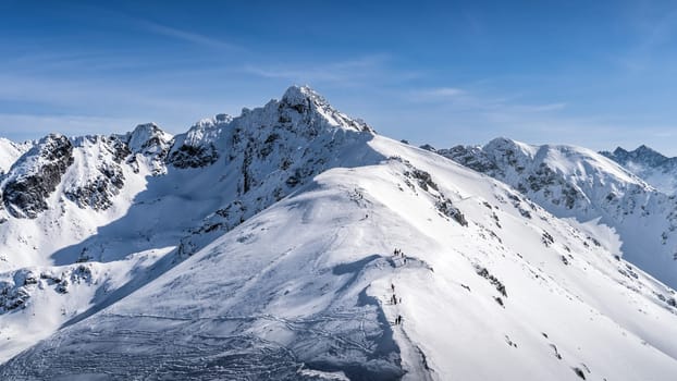 View from Kasprowy Wierch on adventurers climbing on Swinica mountain peak at winter. Tatra Mountains range with snow capped mountain peaks, Poland