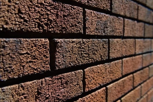 4 - Abstract selective focus side view of harshly lit red brick wall. Lines converge into the blurred distance. Lit by bright sunlight.