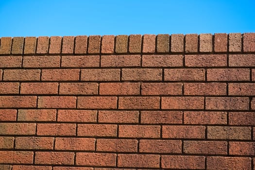 5 - Slanted view of red brick wall on a very bright and sunny day. Red color pops and stands out against the blue sky background. Colorful texture