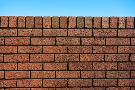 6 - Plain red brick wall background against a bright blue sky background. Sunny summer day. Abstract rough texture with straight dark shadow lines.