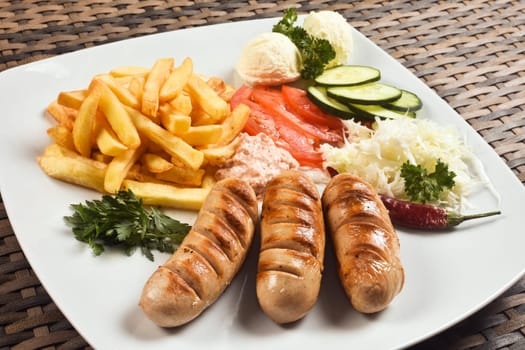 Fast food meat meal with German sausage, french fries and mixed vegetable garnish.