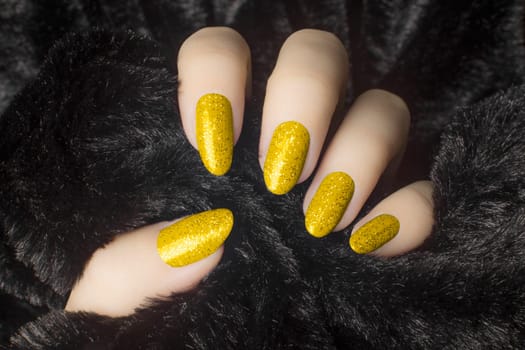 Female hand with glittered yellow nails is holding black fur, manicure and nail care concept.