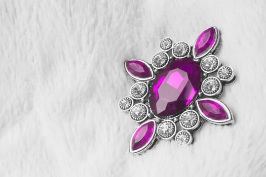 Beautiful luxurious brooch jewel or jewelry with pink gem on white fur background.
