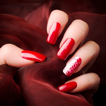 Female hand with beautiful red nails on red background, nail care and manicure concept.