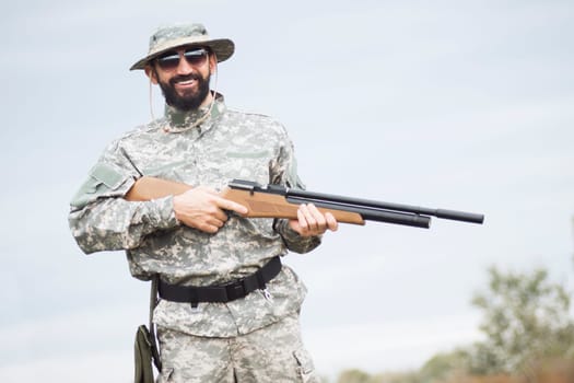 Portrait of smiling hunter or army soldier in military uniform with rifle in nature.