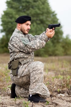The army soldier in military uniform is holding pistol and aiming outdoors in nature.