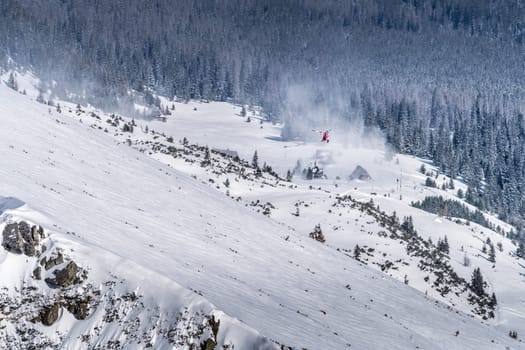 Helicopter rescue crew providing service in High Tatra Mountains. Medical helicopter hovering over mountain shelter, Poland