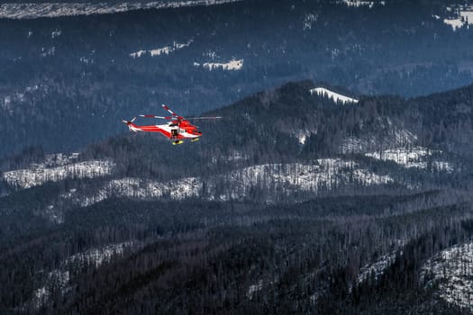 Red and White helicopter, rescue team or crew flying over dark forest in High Tatra Mountains, providing rescue service, Poland