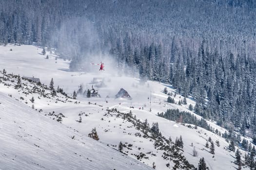 Helicopter rescue crew providing service in High Tatra Mountains. Medical helicopter hovering over mountain shelter, Poland