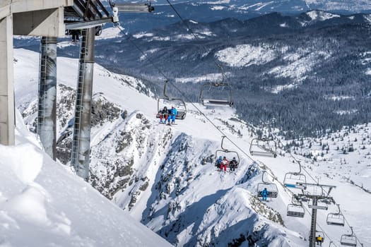 Skiers and snowboarders going up the ski slopes of Kasprowy Wierch on a ski lift. Winter holidays in High Tatra Mountains, Poland