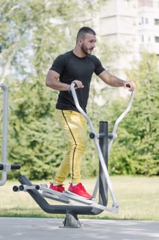 The young sporty guy is exercising on gym equipment outdoors in the park.