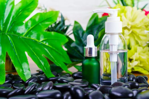 Thai Spa massage setting with serum oil bottle dropper mock up or essential oil on black stone against green leave background