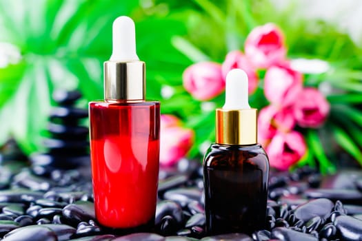 Cosmetic glass bottle for essential oils on black stone against the background of a flowering. Spa still life with natural serums in glass bottle. Dropper bottle mock up