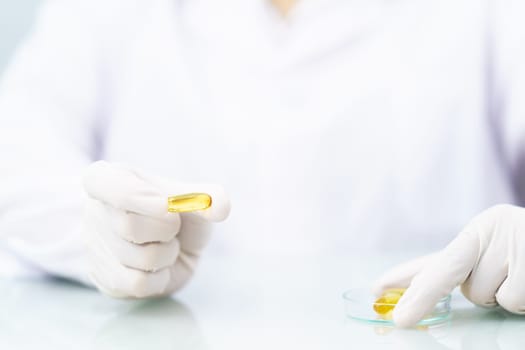 Close up Scientist hands putting in nitrile latex gloves holding Omega 3 capsule in labcoat doing experiments in lab